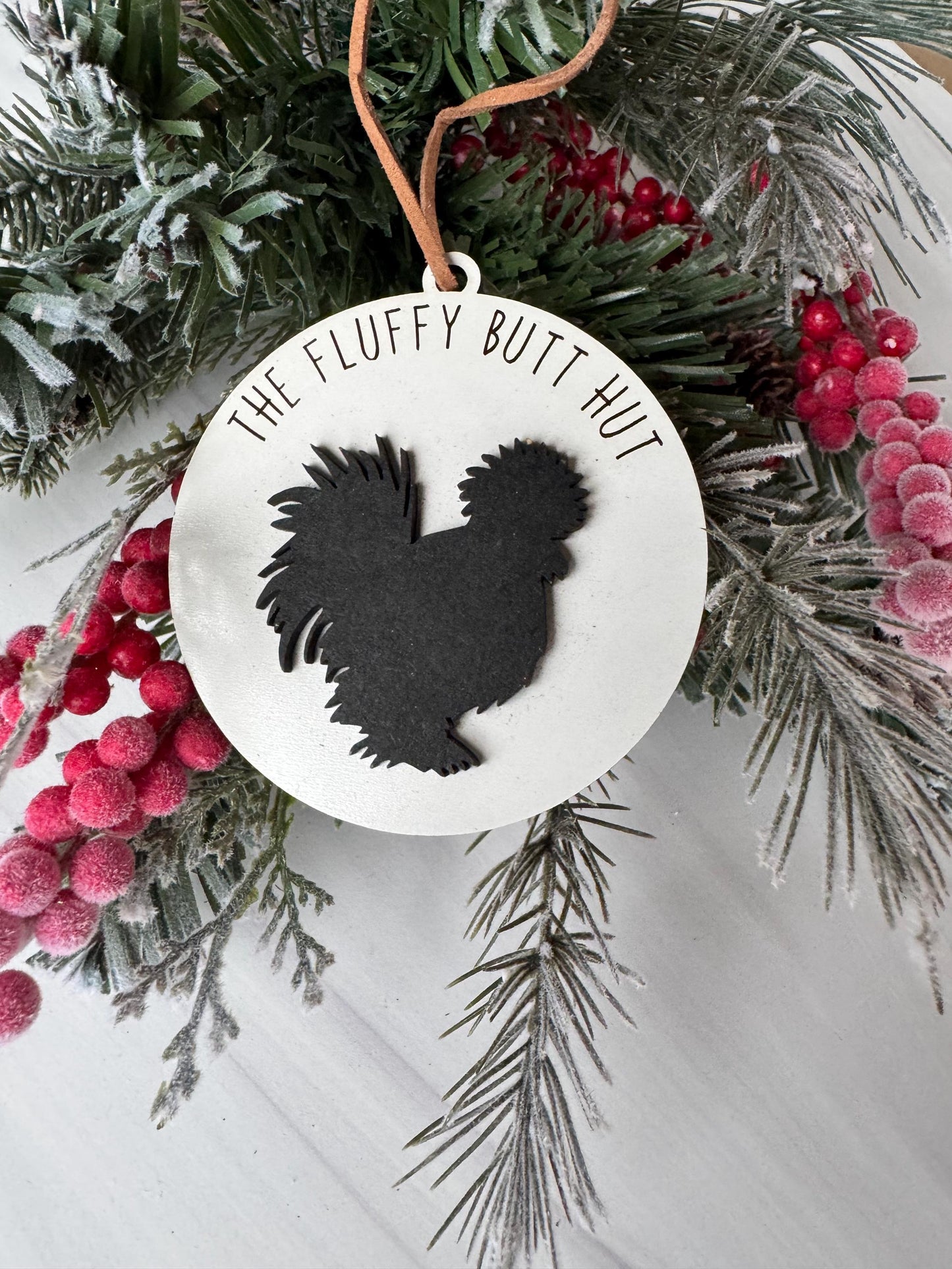 A white ornament with a black silhouette of a turkey is displayed on a branch with red berries and pine needles.
