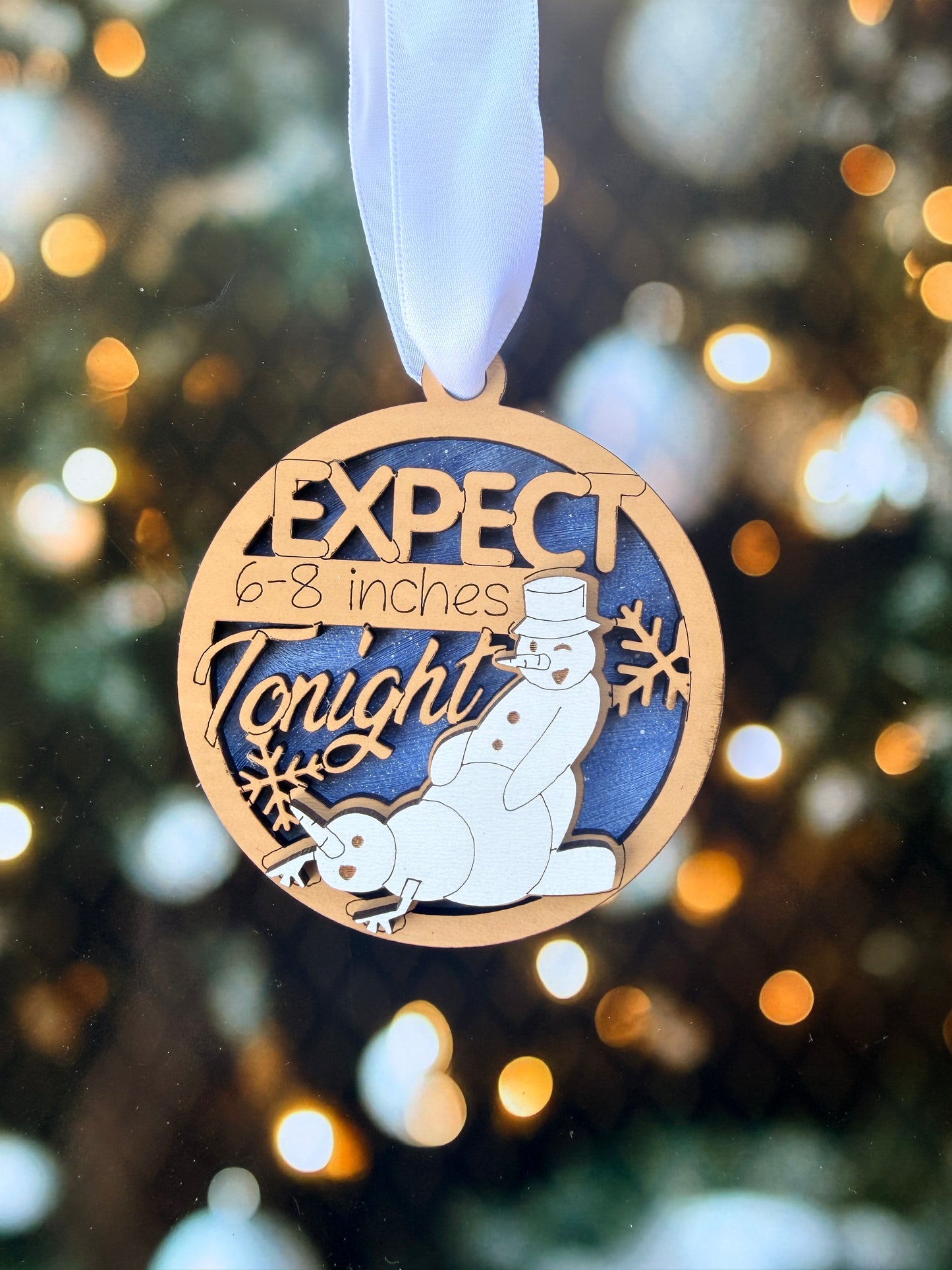 A wooden ornament with a snowman design and the text "EXPECT 6-8 INCHS TOUGH" on it.