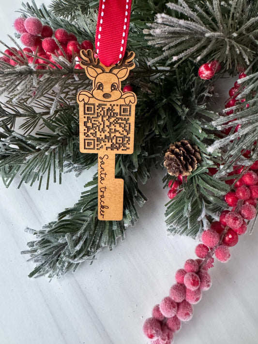 A Christmas ornament with a QR code and the word &quot;Santa Tracker&quot; is displayed on a pine branch with red berries.