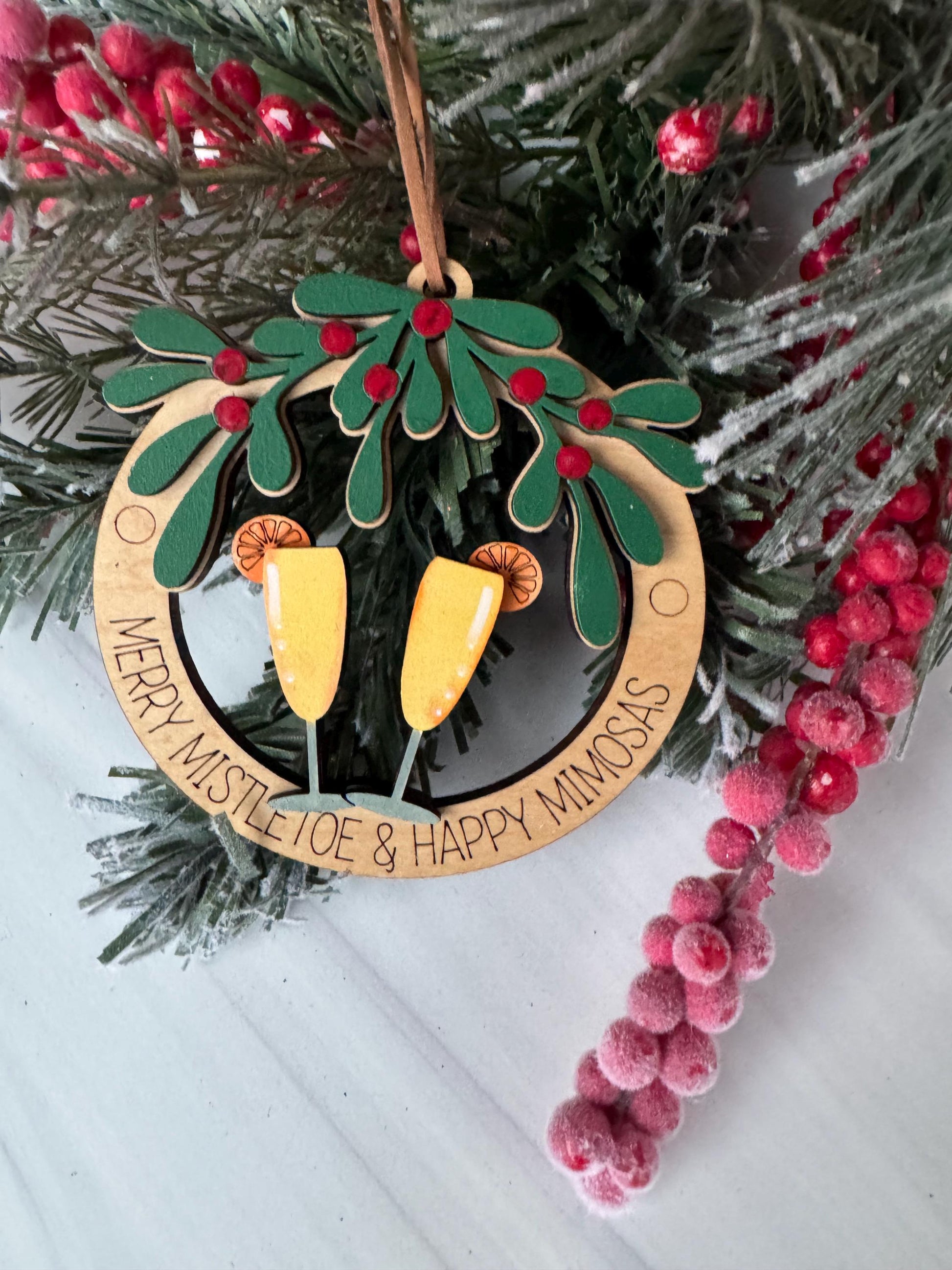A wooden ornament with a festive design, surrounded by a wreath of greenery and red berries, with the text &quot;Merry Mistle & Happy Joe&quot; displayed on it.