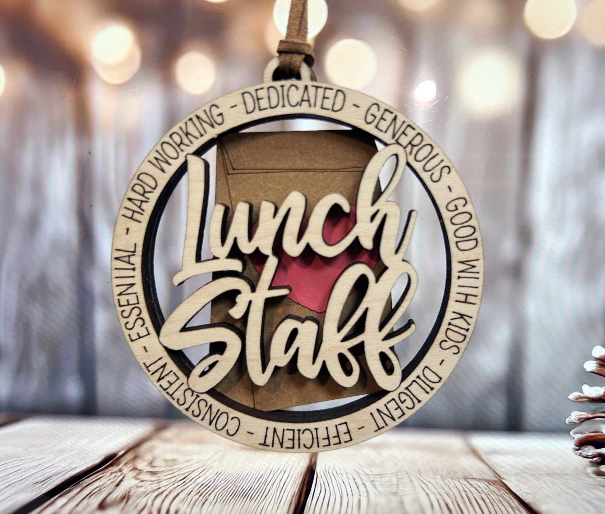 A wooden ornament with the word "Lunch Staff" written on it, surrounded by the words "Hard working - Dedicated - Generous - Good with kids - Consistent - Effortless - Flexible" in a circular frame.