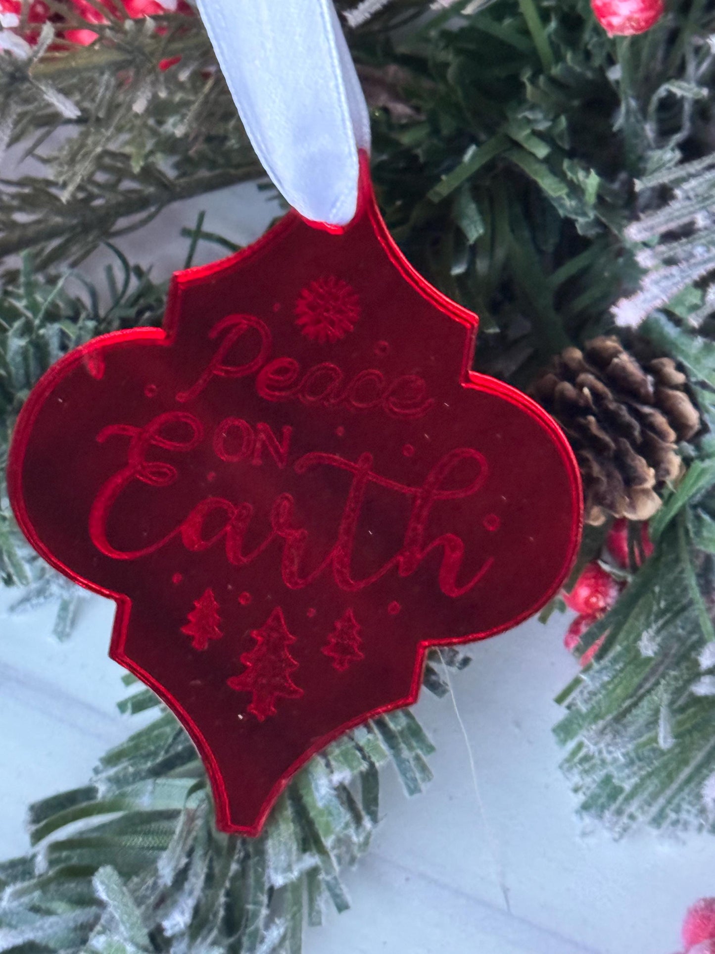 A red ornament with the text &quot;Peace on Earth&quot; is hanging on a Christmas tree, surrounded by pine branches and red berries.