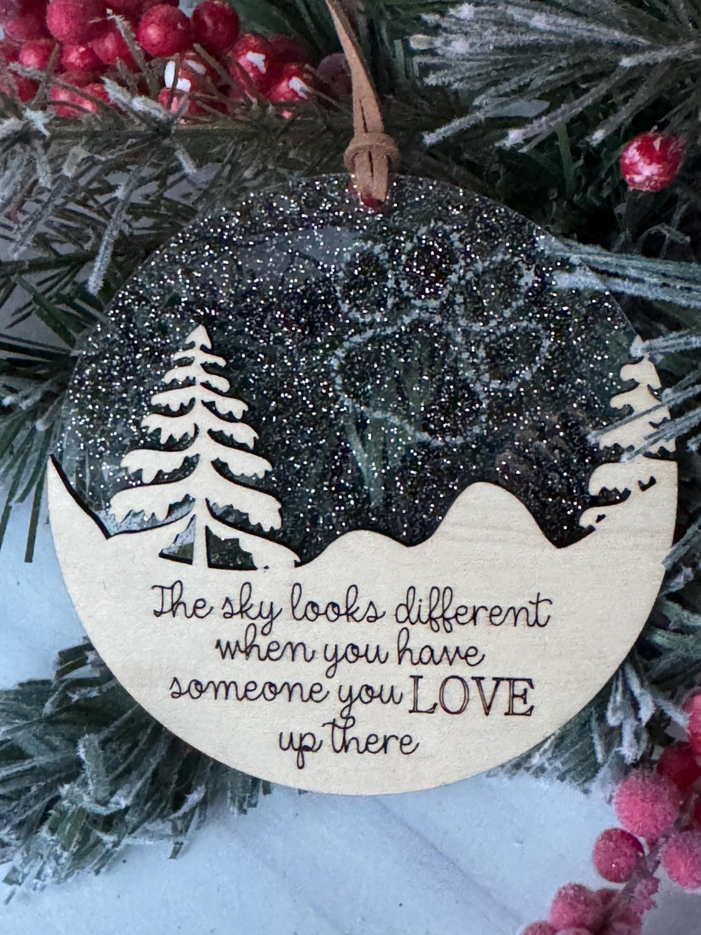 A wooden ornament with a snowflake design and the text "The sky looks different when you have someone you love up there" is displayed on a Christmas tree.