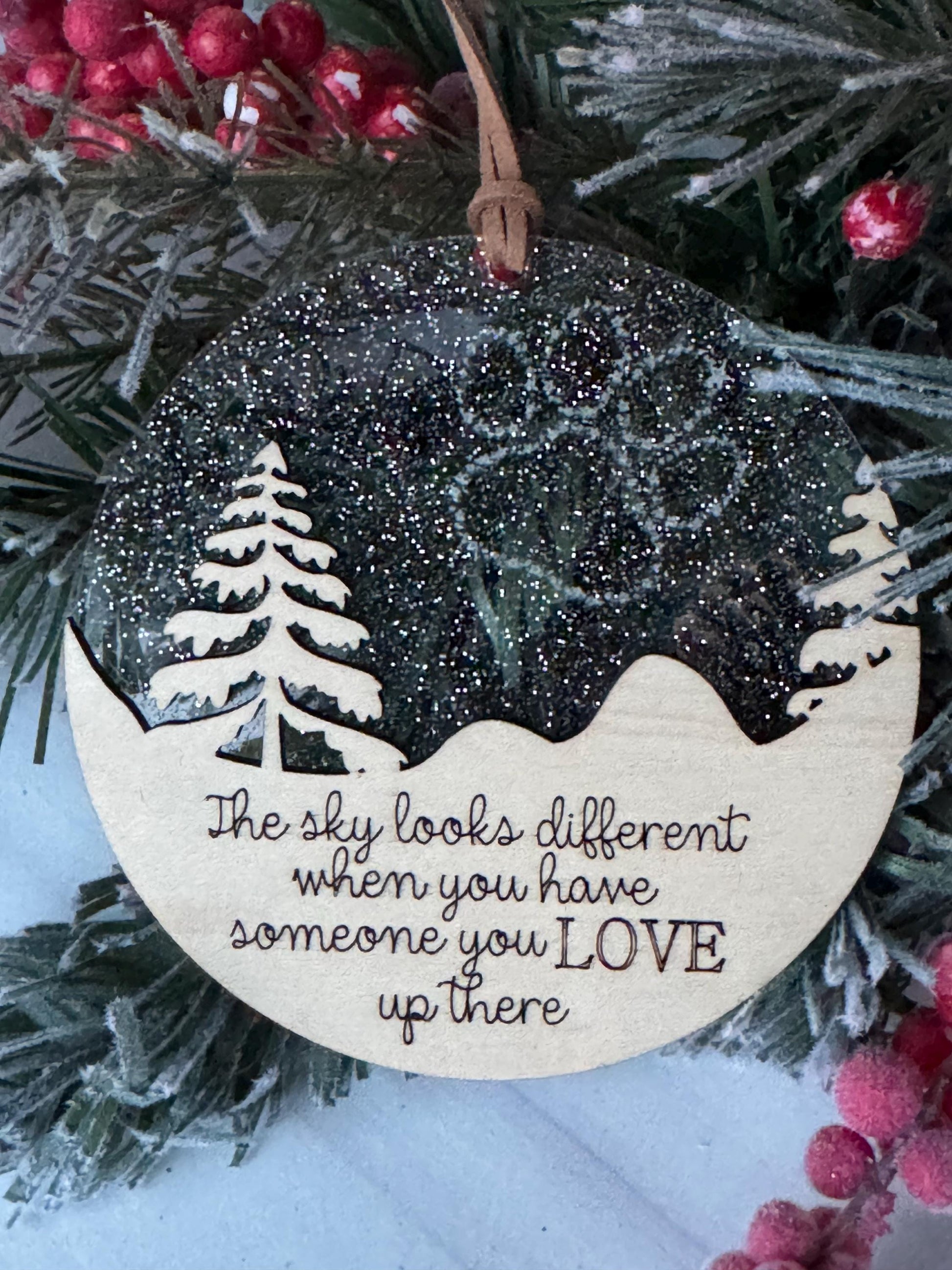 A wooden ornament with a snowflake design and the text "The sky looks different when you have someone you love up there" is displayed on a Christmas tree.