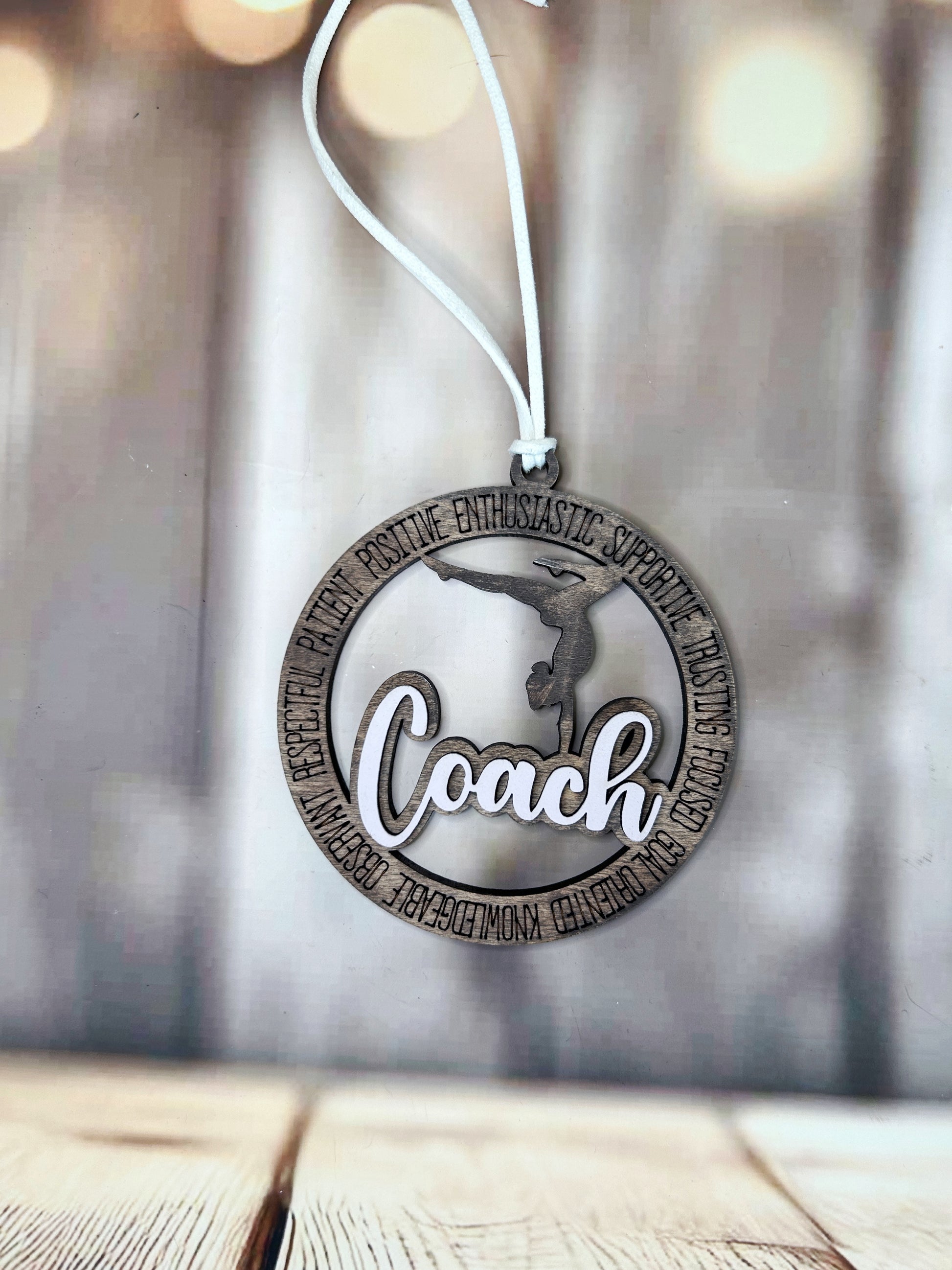 A wooden ornament with the word "Coach" written on it, hanging from a string.