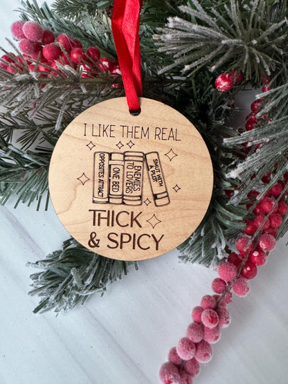 A wooden ornament with a red ribbon, featuring a humorous text and an illustration of a stack of books.