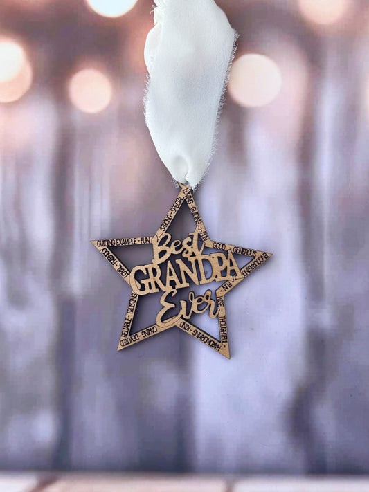 A wooden star-shaped ornament with the text "Best Grandpa Ever" written on it, hanging against a blurred background with a white ribbon.