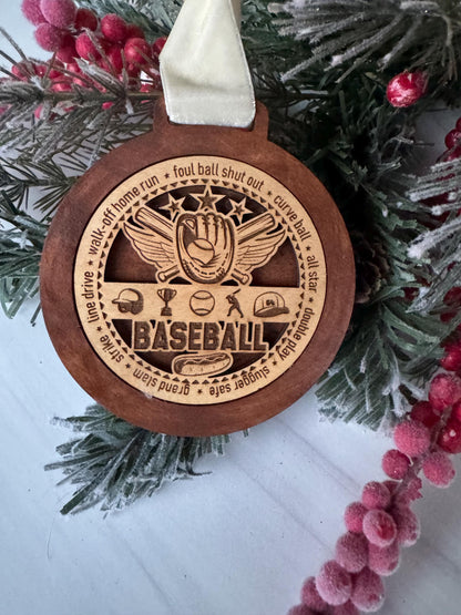 A wooden baseball ornament with a carved design, featuring a baseball glove and a baseball, is displayed on a pine branch with red berries.