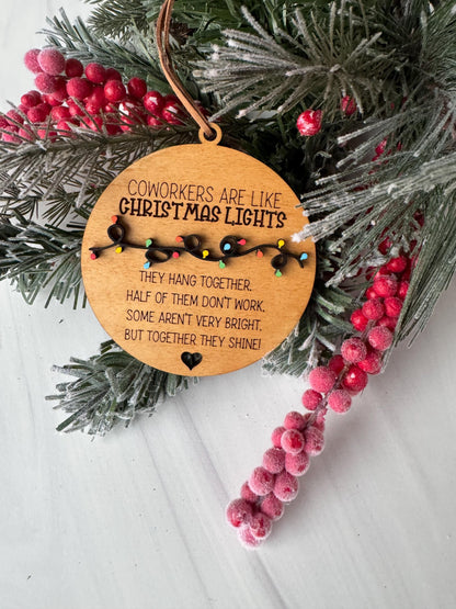 A wooden ornament with a message about coworkers being like Christmas lights, surrounded by pine branches, red berries, and a white background.
