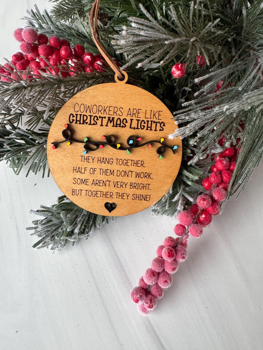 A wooden ornament with a message about coworkers being like Christmas lights, surrounded by pine branches, red berries, and a white background.