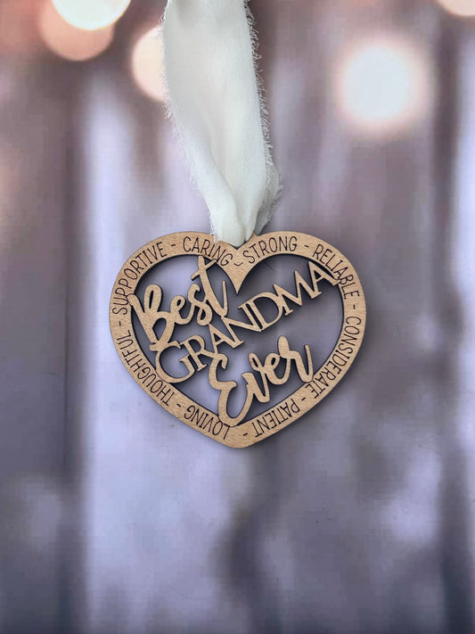 A heart-shaped ornament with the words "Best Grandma Ever" written on it, hanging against a blurred background.