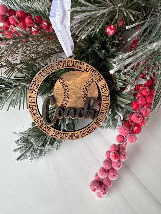 A wooden ornament with the word "Coach" engraved on it, surrounded by a wreath of pine branches and red berries.