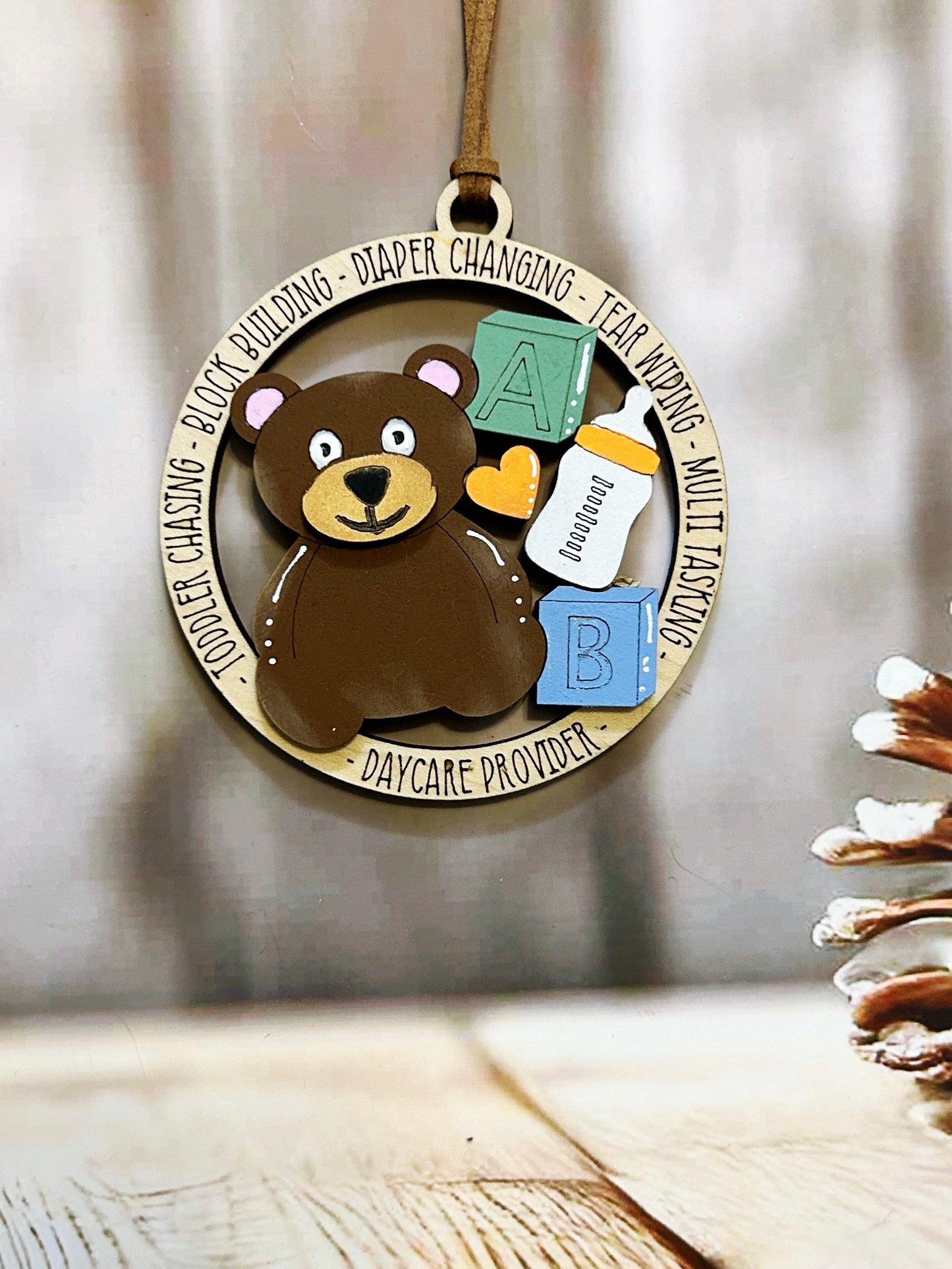 A wooden ornament featuring a brown teddy bear surrounded by baby-related items, such as a bottle and a pacifier, with the text "Daycare Provider" around the edges.