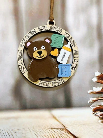 A wooden ornament featuring a brown teddy bear surrounded by baby-related items, such as a bottle and a pacifier, with the text "Daycare Provider" around the edges.