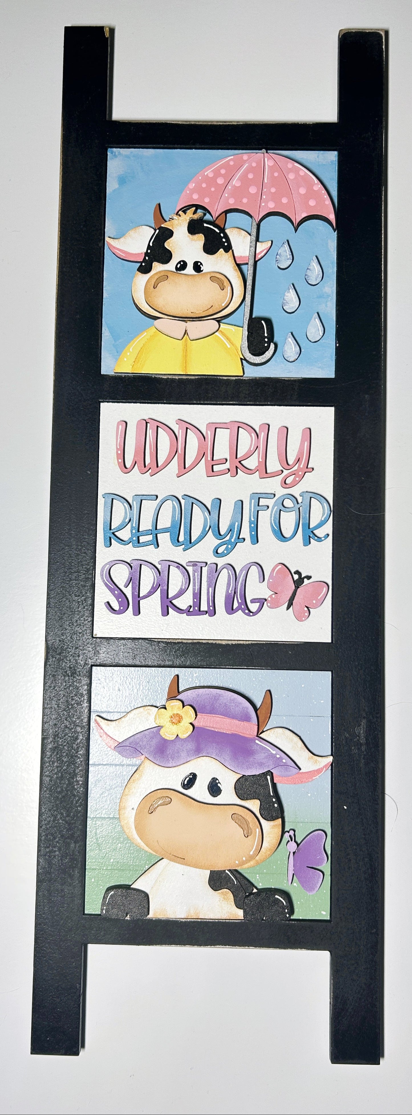 Decorative ladder with cartoon cow illustrations and 'Udderly Ready for Spring' text on a white background

