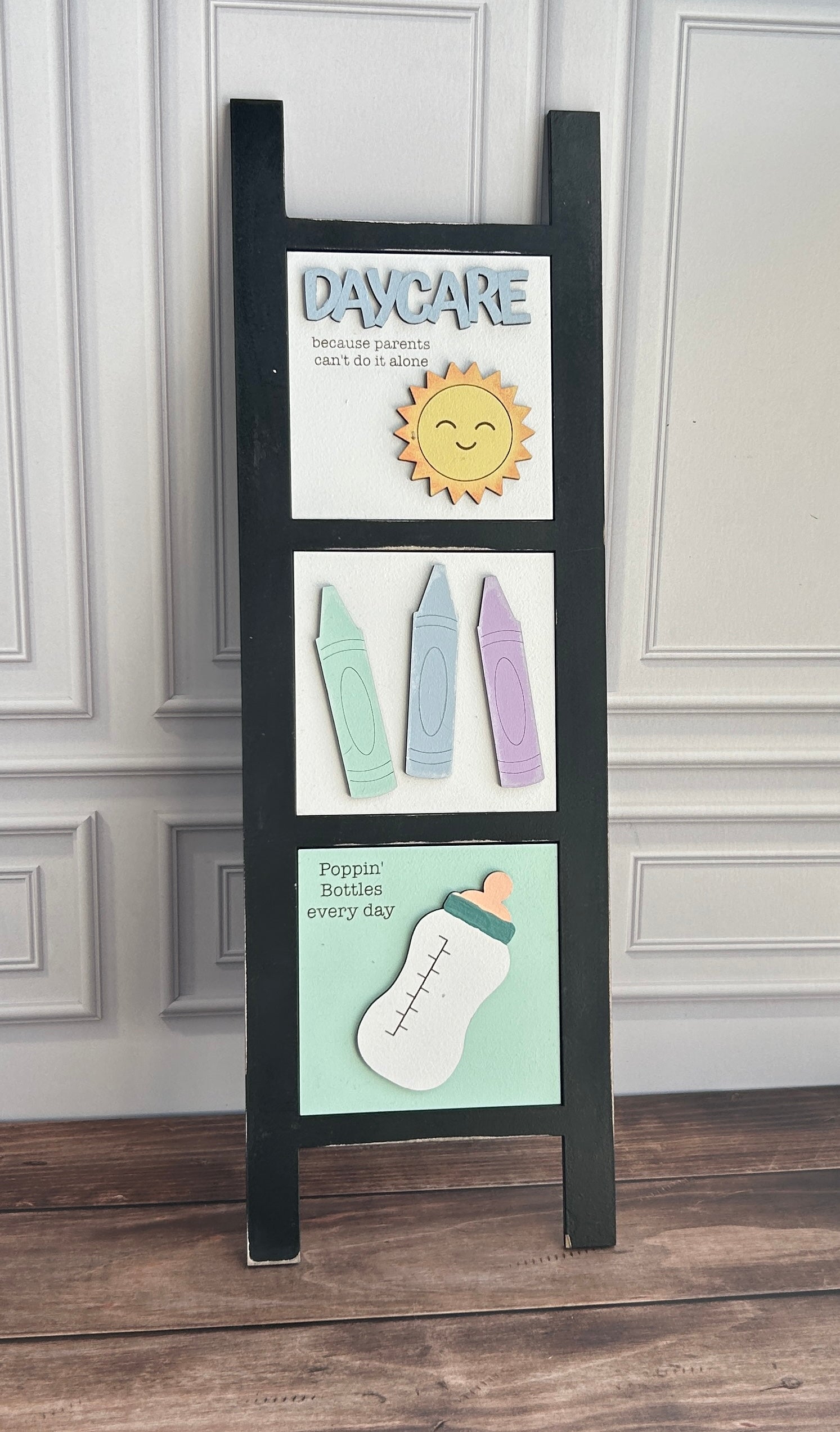 Black wooden sign with colorful illustrations and text on a white paneled wall.