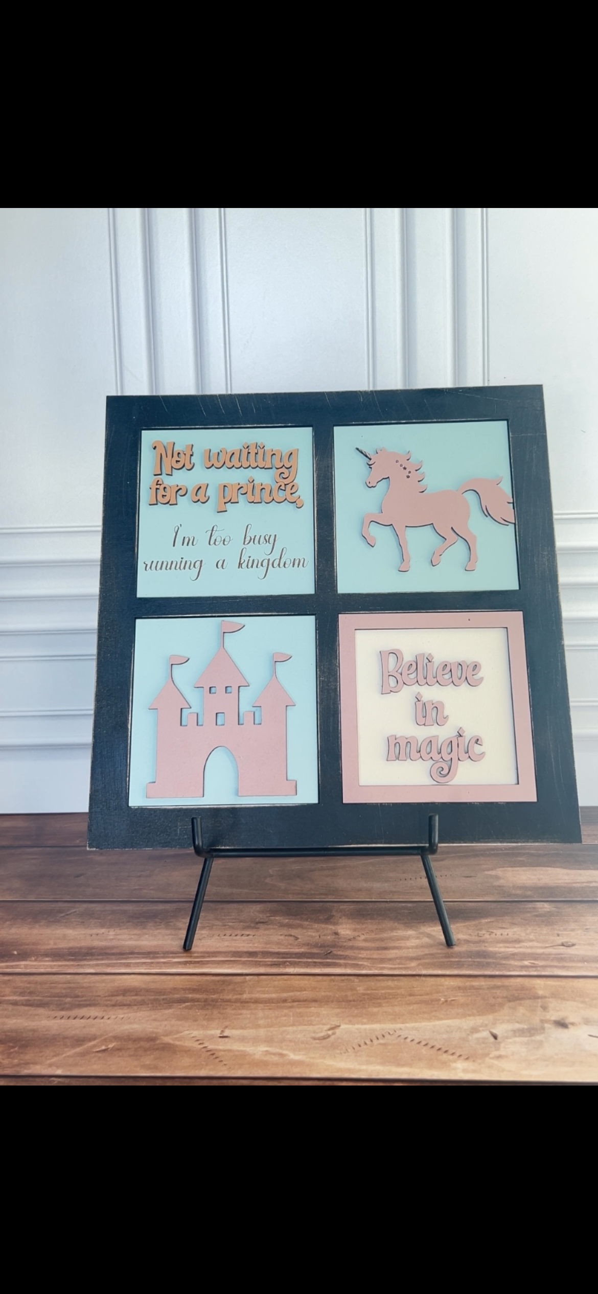 Decorative sign with unicorn and castle illustrations on a wooden floor.