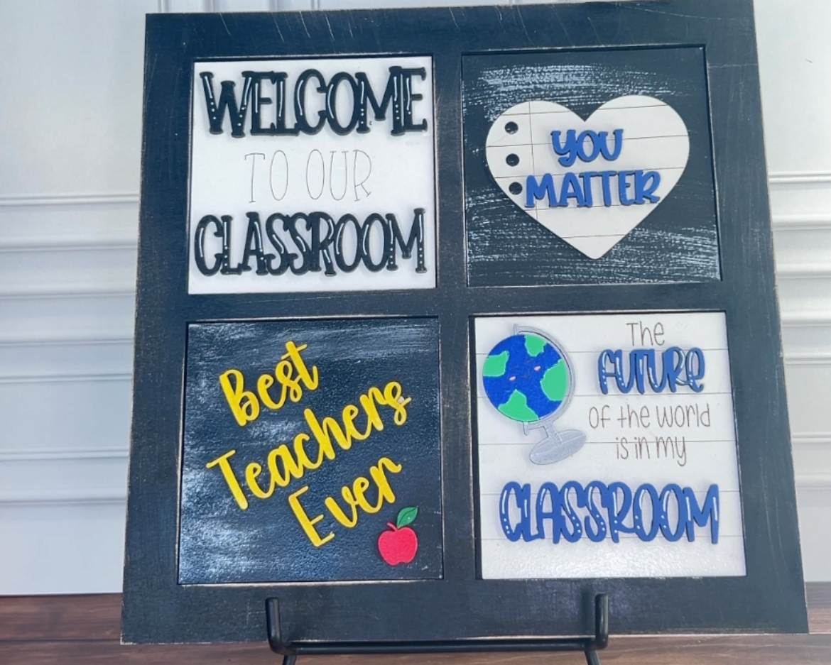 Decorative signboard with motivational phrases on a stand against a white wall.