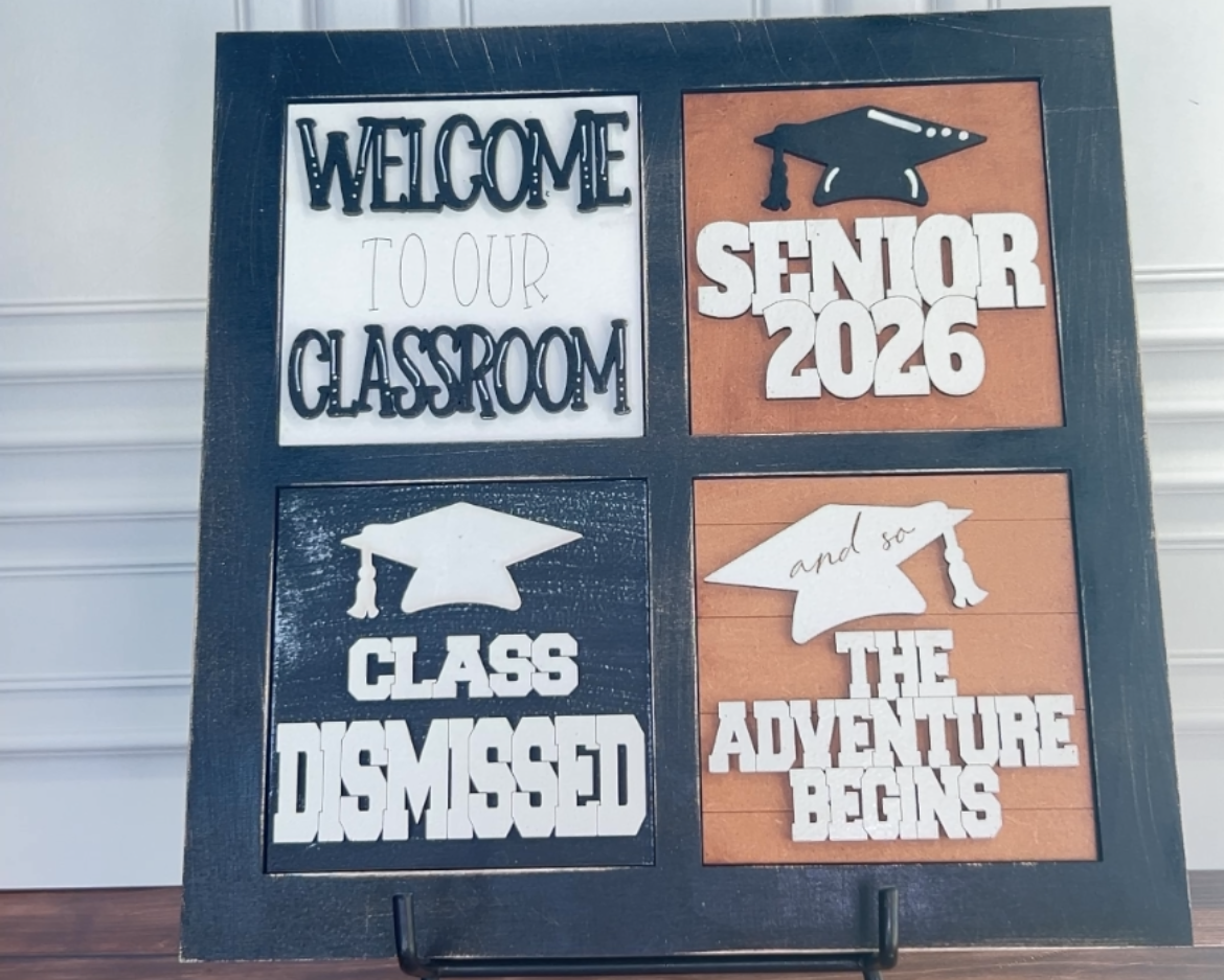 Graduation-themed sign with text on a stand against a white wall.