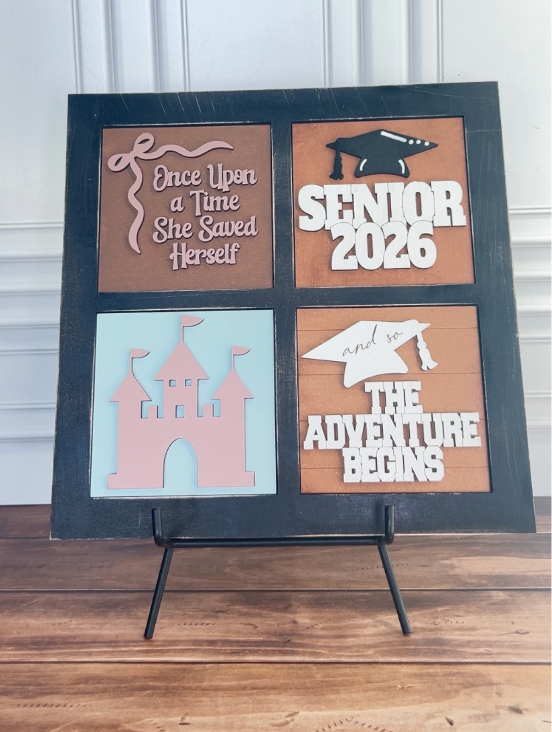 Decorative sign with cut-out phrases 'Once Upon a Time She Saved Herself', 'Senior 2026', 'The Adventure Begins' on a stand.