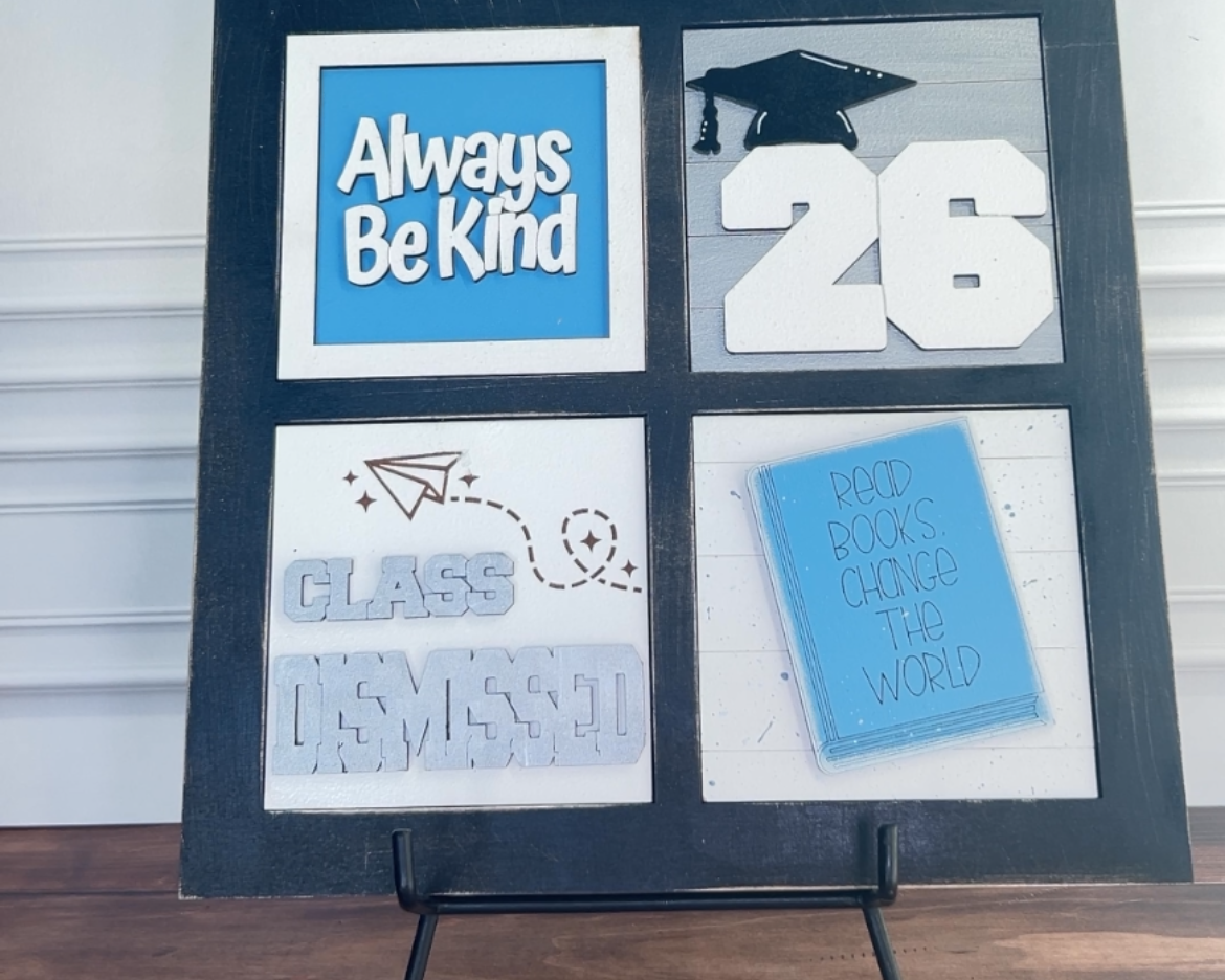 Graduation-themed decorative board with text and images on a stand against a white wall.