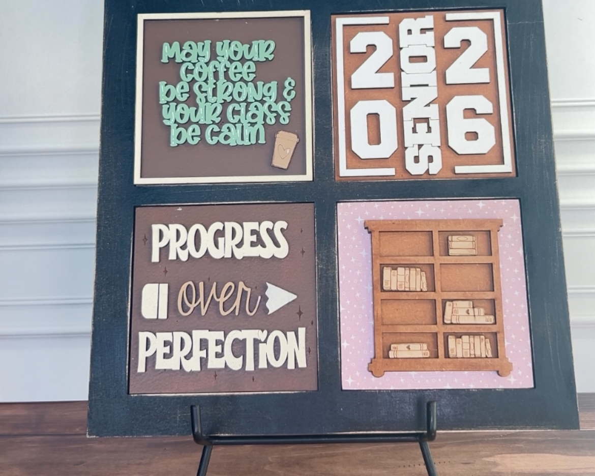 Decorative sign with motivational phrases and a calendar on a stand against a white wall.