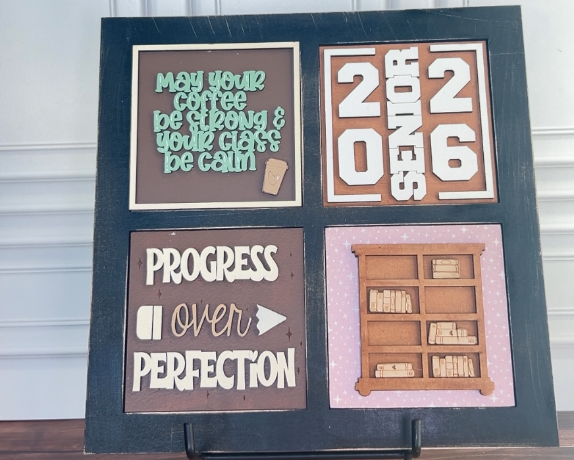 Decorative sign with motivational phrases and a calendar on a stand against a white wall.