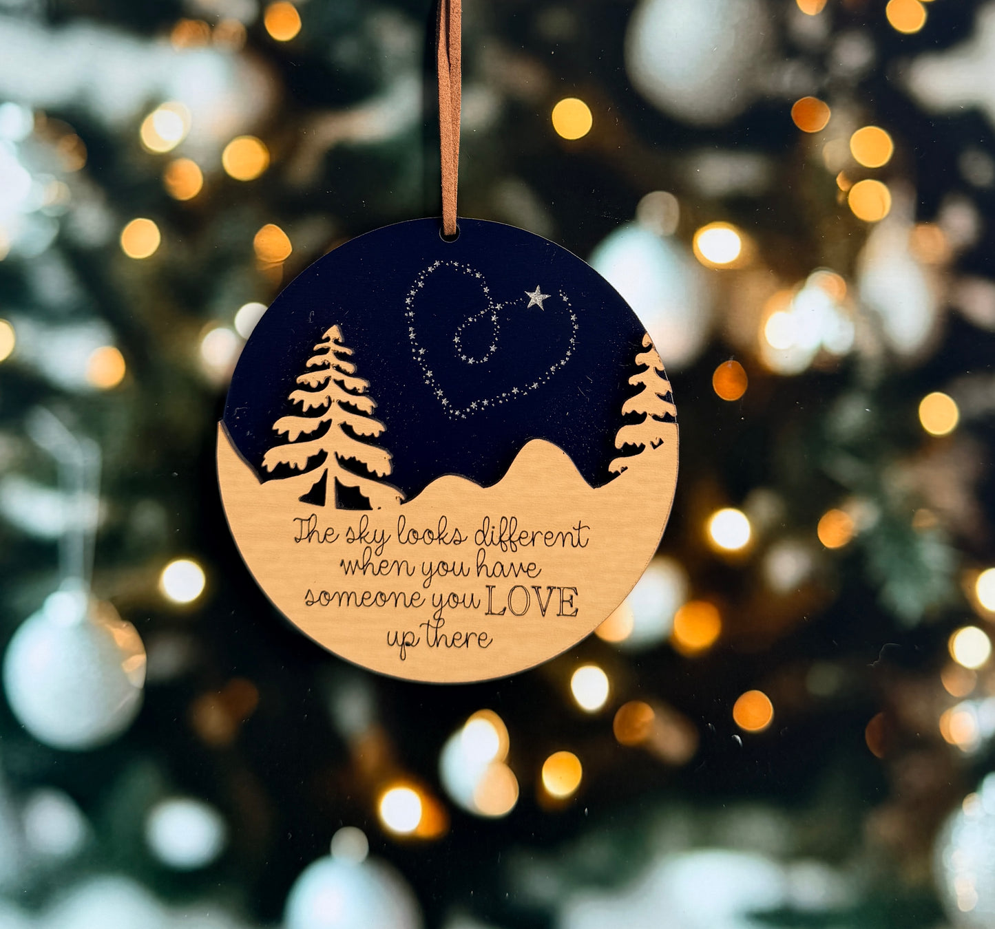A round ornament with a night sky scene and a heart symbol hangs against a background of blurred lights, conveying a sense of love and connection.