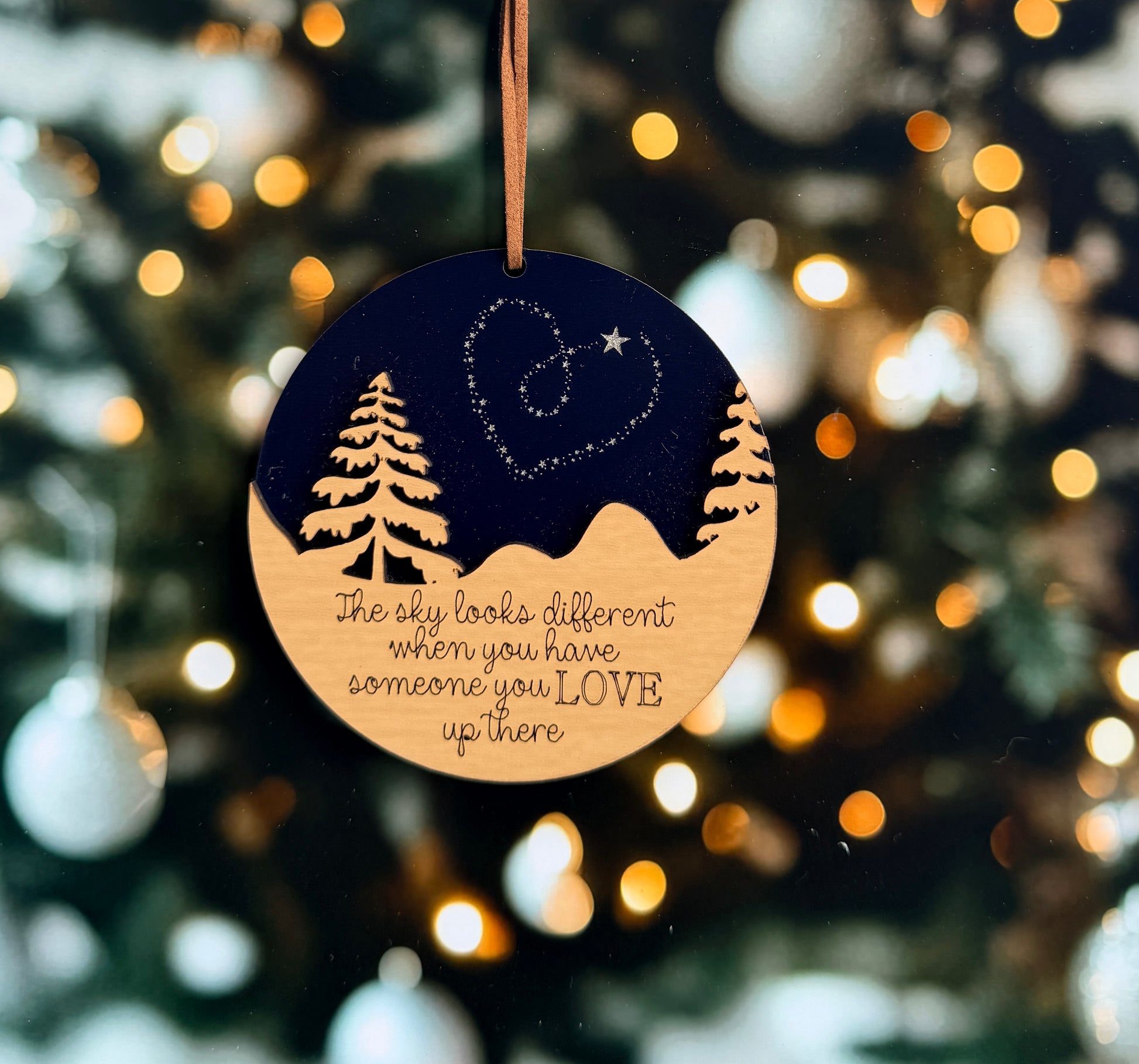 A round ornament with a night sky scene and a heart symbol hangs against a background of blurred lights, conveying a sense of love and connection.