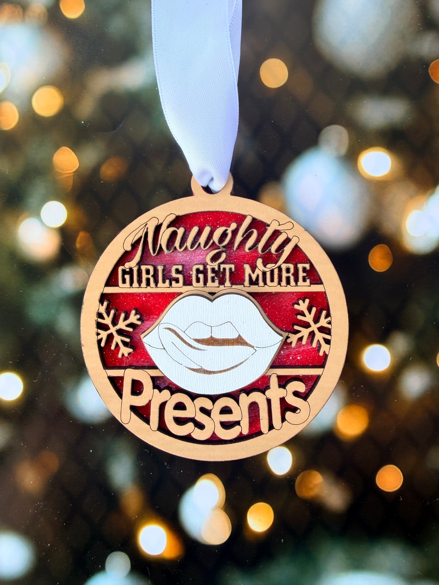 A close-up of a round ornament with a ribbon, featuring the text "Naughty Girls Get More" and a snowflake design.