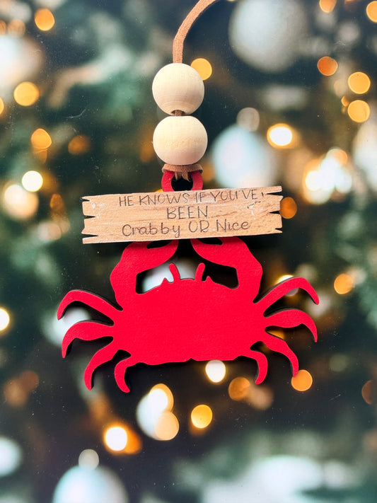 A red crab ornament is attached to a wooden stick with a message written on it, set against a blurred background with twinkling lights.