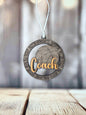 A wooden ornament with the word "Coach" written on it, hanging on a string against a blurred background.