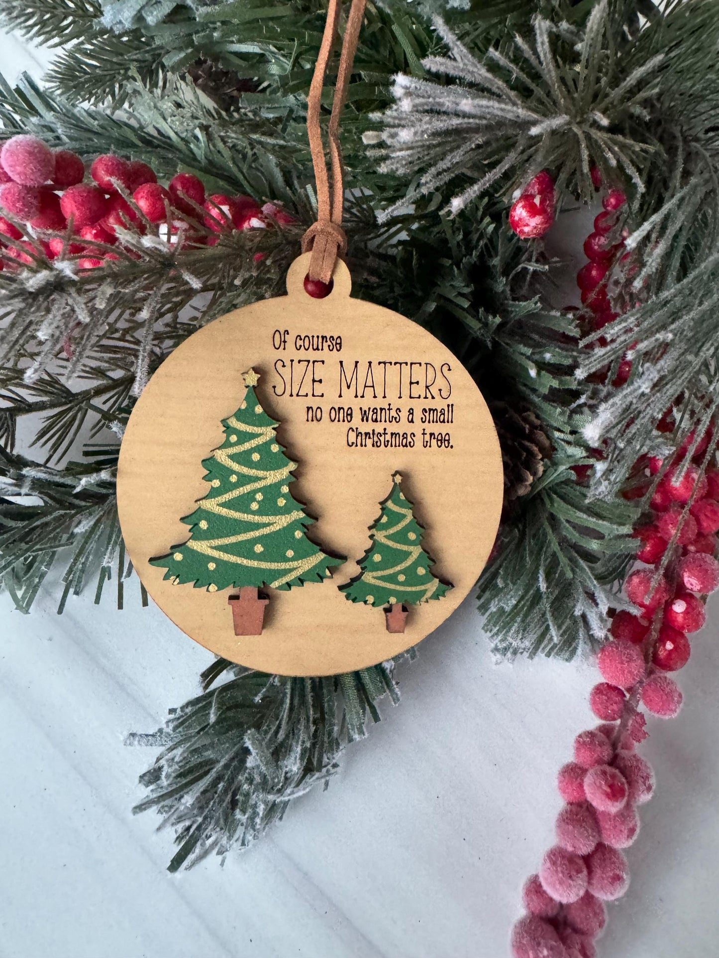 A wooden ornament with a Christmas tree design, hanging on a branch with red berries.