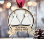 A wooden ornament with two white dress silhouettes hanging from a red ribbon, and a banner below that reads "Our first Christmas as MRS & MRS".