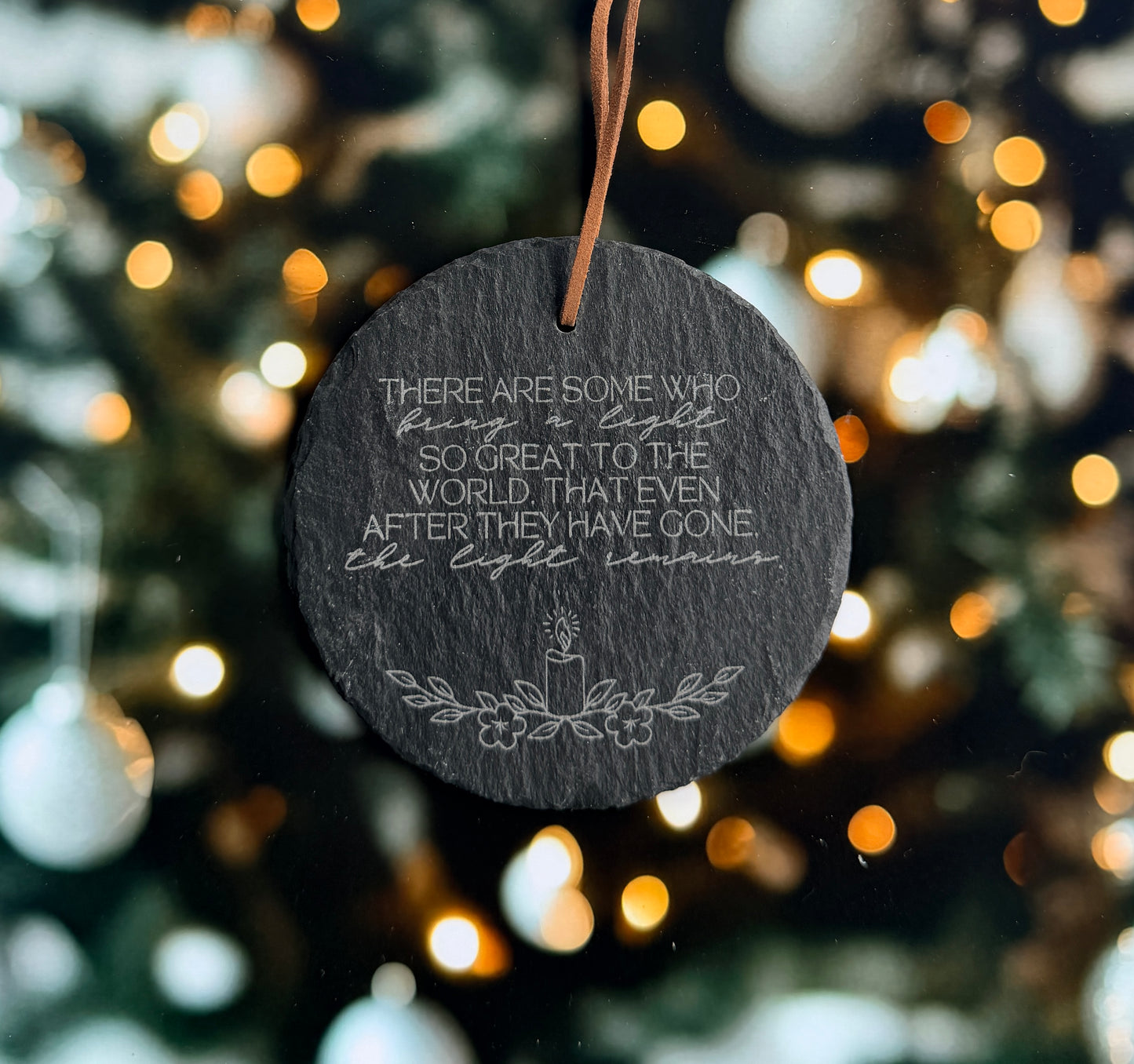 A black slate ornament with a quote about light and the world, surrounded by a blurred background of Christmas lights.