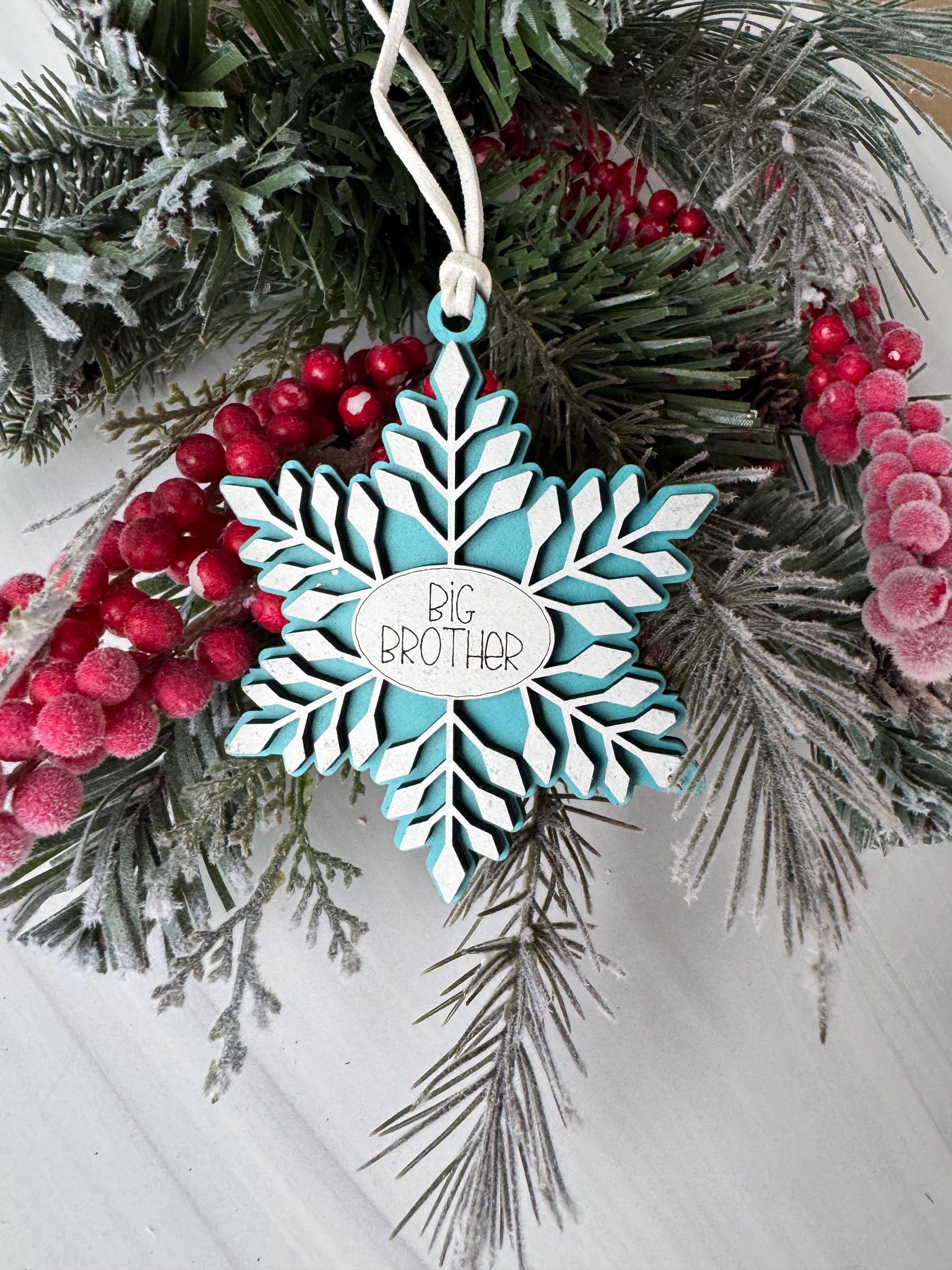 A blue snowflake ornament with the text &quot;BIRTH BROTHER&quot; is displayed among pine branches, berries, and pine needles.