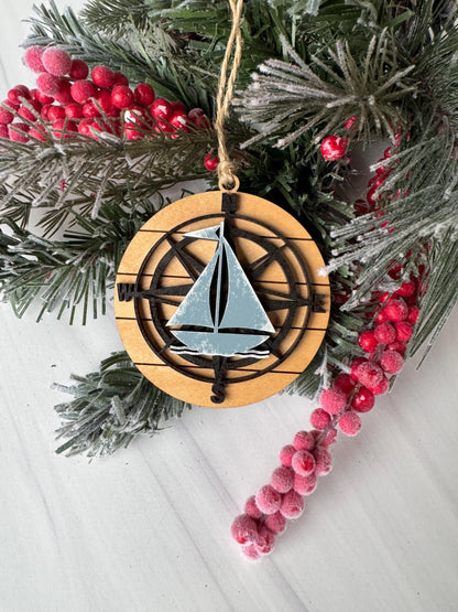 A wooden ornament with a compass design is surrounded by a wreath of pine branches and red berries on a white surface.