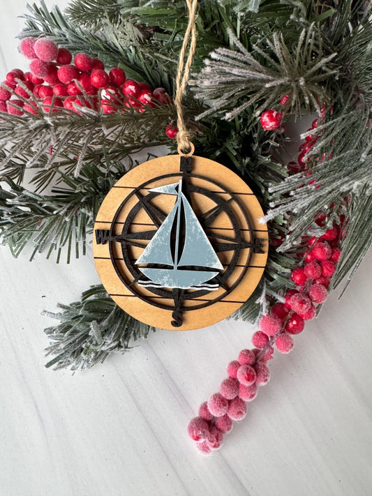 A wooden ornament with a compass design is surrounded by a wreath of pine branches and red berries on a white surface.