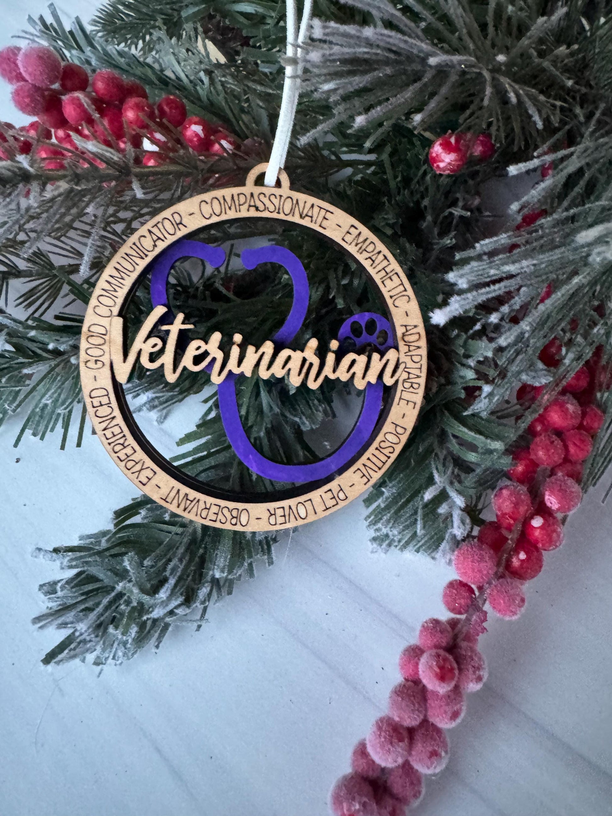 A Christmas ornament with the word "Veterinarian" written on it, surrounded by pine branches and red berries.