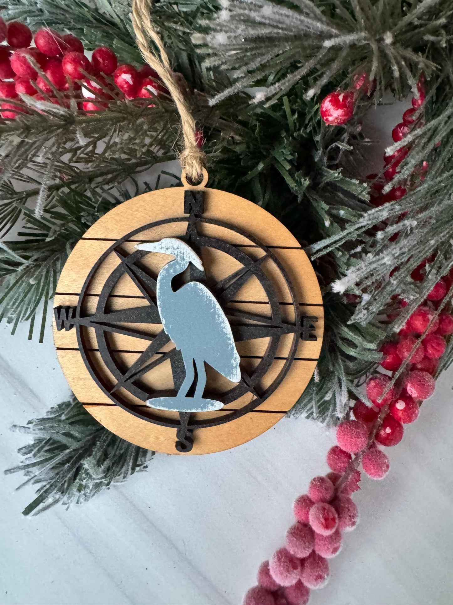 A wooden ornament with a compass design, surrounded by pine branches and red berries, creating a festive holiday scene.