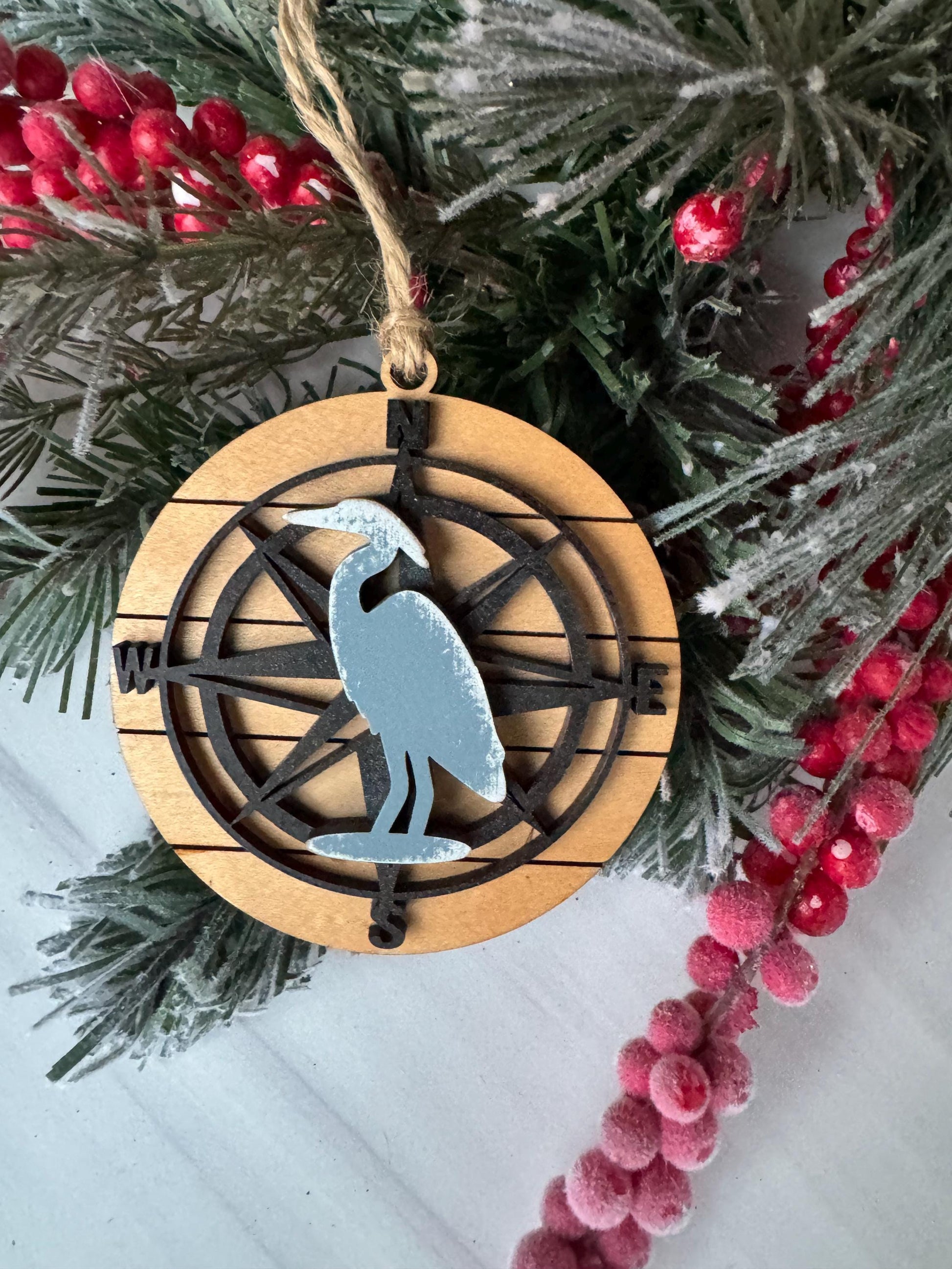 A wooden ornament with a compass design, surrounded by pine branches and red berries, creating a festive holiday scene.