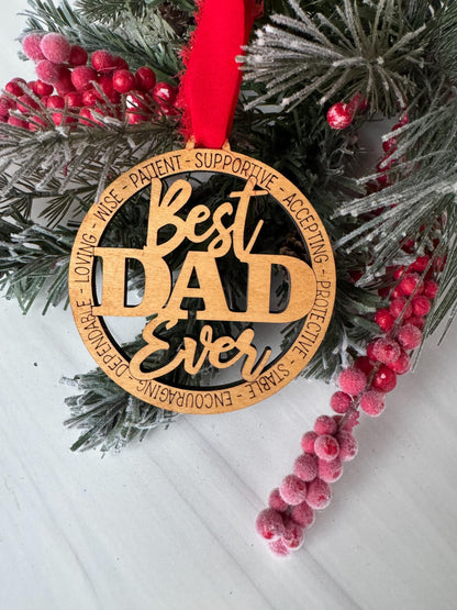 A wooden ornament with the text "Best Dad Ever" is displayed on a pine branch with red berries.