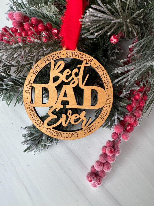 A wooden ornament with the text "Best Dad Ever" is displayed on a pine branch with red berries.