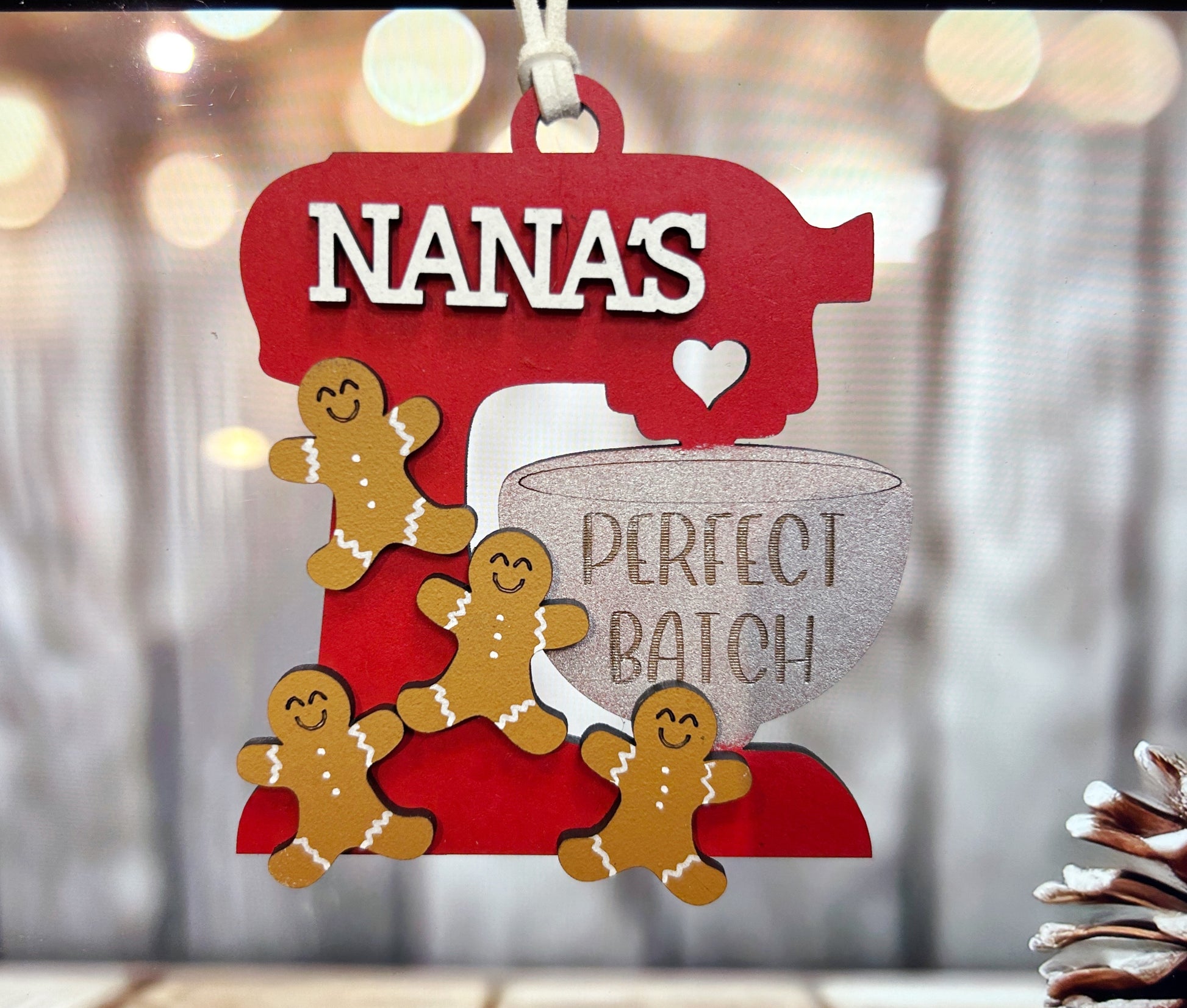 A red ornament with a red mixer and three gingerbread men, with the word "NANA's" written above them.