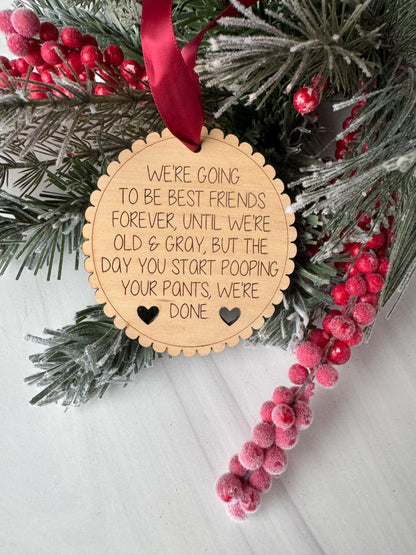 A wooden ornament with a message about being the best friend, placed among pine branches and red berries on a white surface.