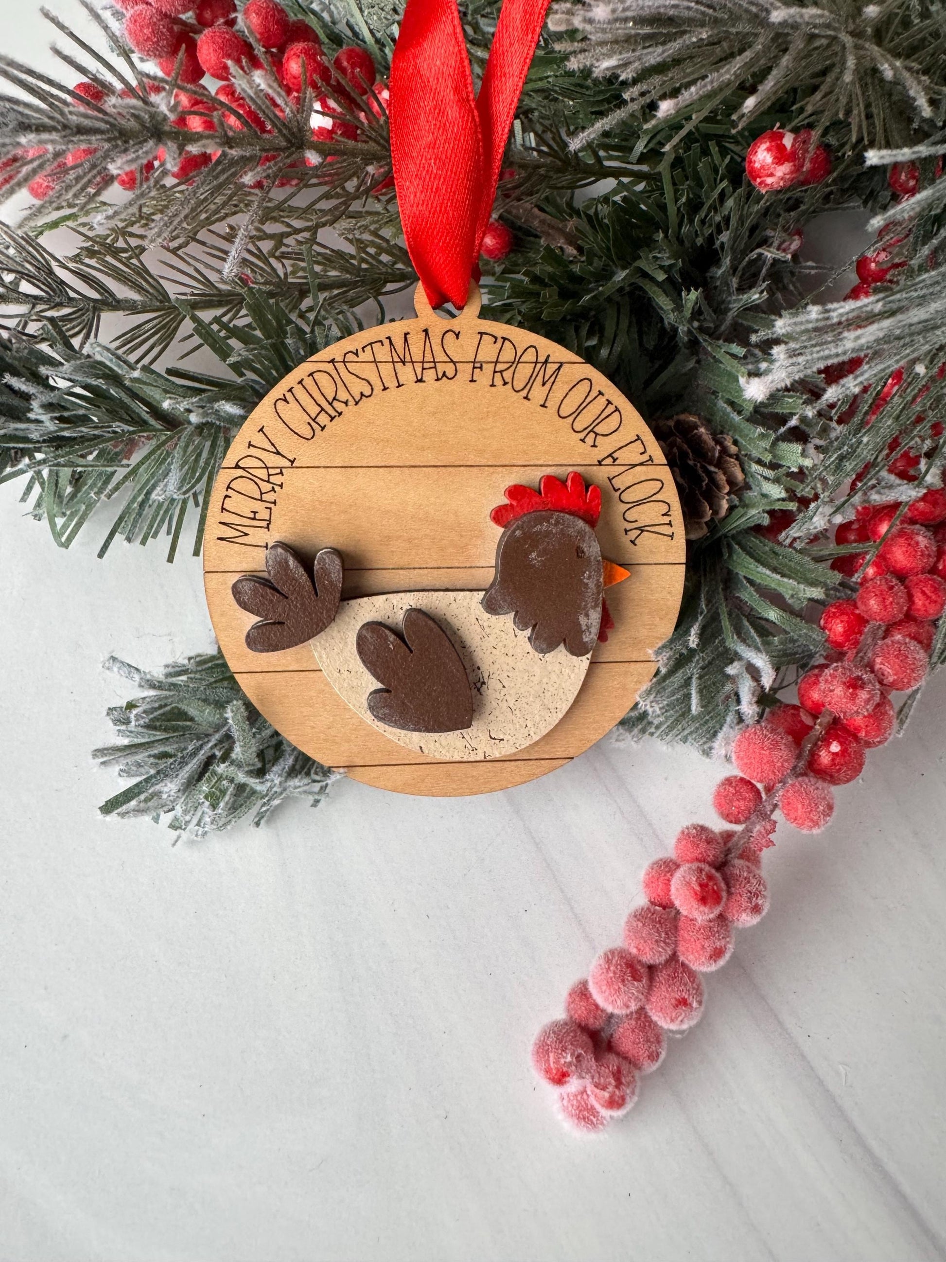 A wooden ornament with a rooster design, surrounded by Christmas decorations such as berries and pine branches.