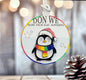 A colorful ornament featuring a penguin wearing a Santa hat and scarf, with the text "DON WE NOW OUR GAY APPAREL" displayed on it.