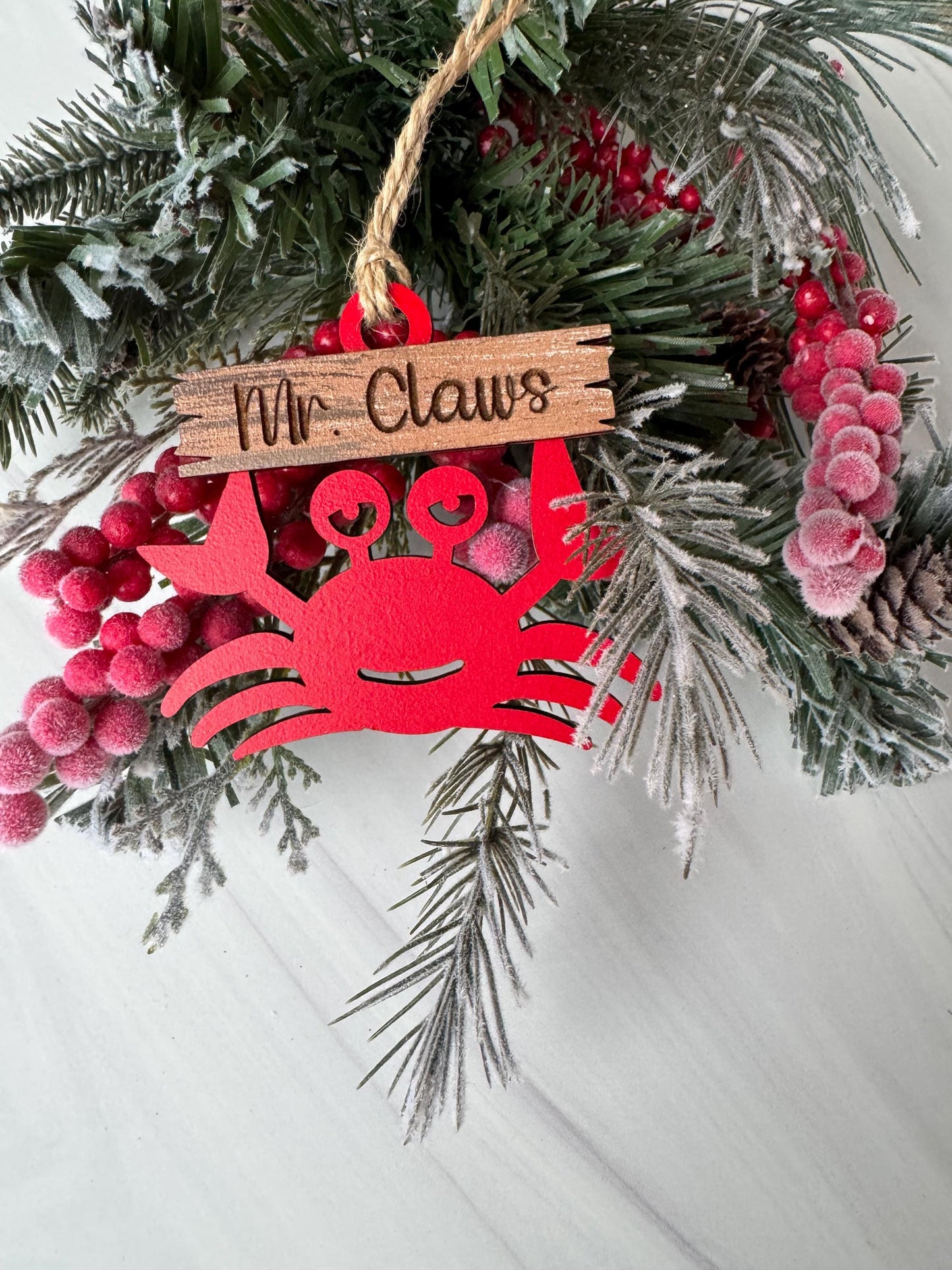A Christmas wreath with pine branches, berries, and a red ornament shaped like a crab.