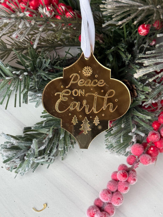 A gold ornament with the text "Peace on Earth" is displayed on a wreath of pine branches and red berries.