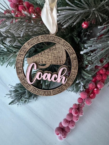 A wooden ornament with the word &quot;Coach&quot; on it, surrounded by a wreath of pine branches and red berries.